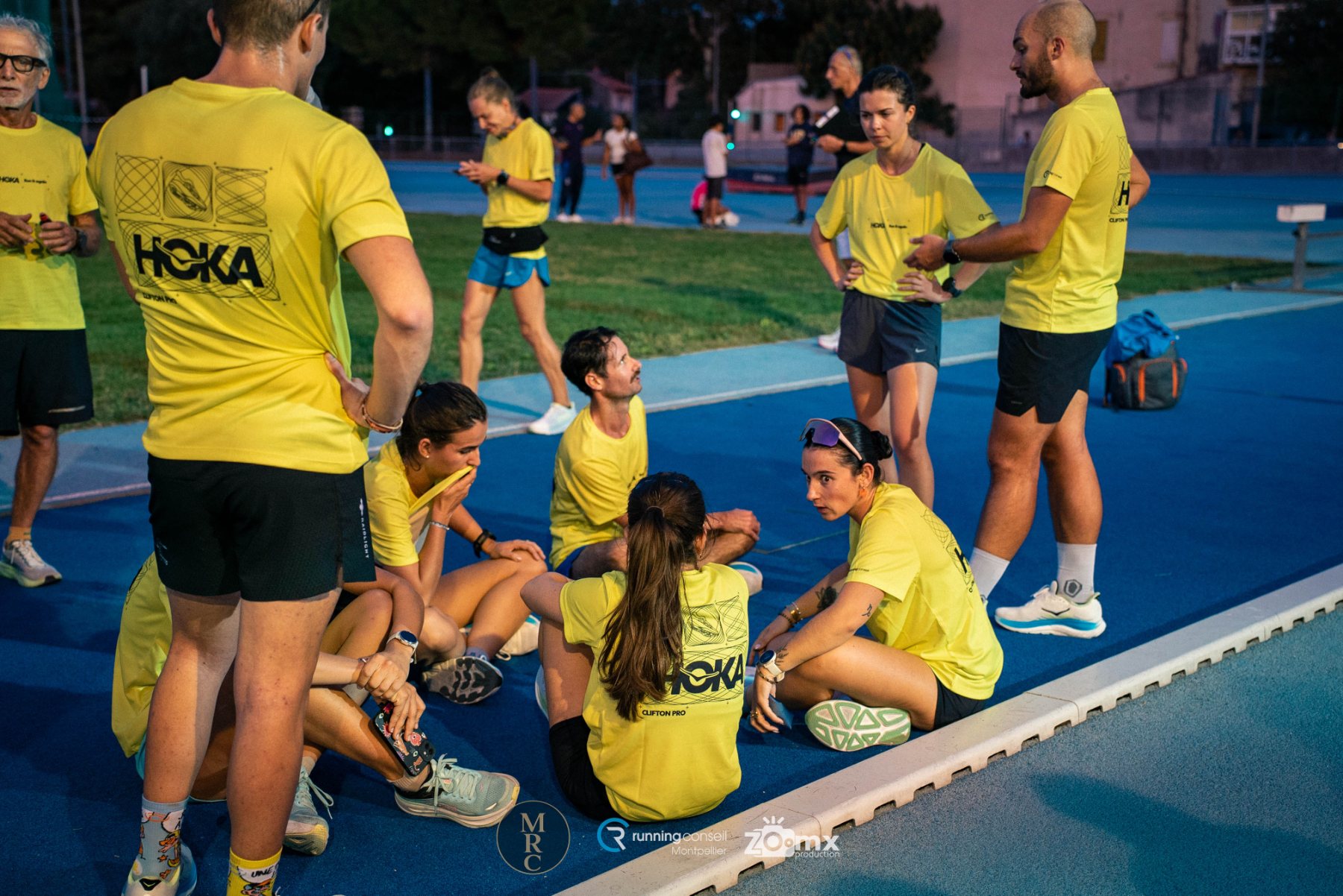 Coach debout briefant un groupe de coureurs assis sur la piste d'athlétisme
